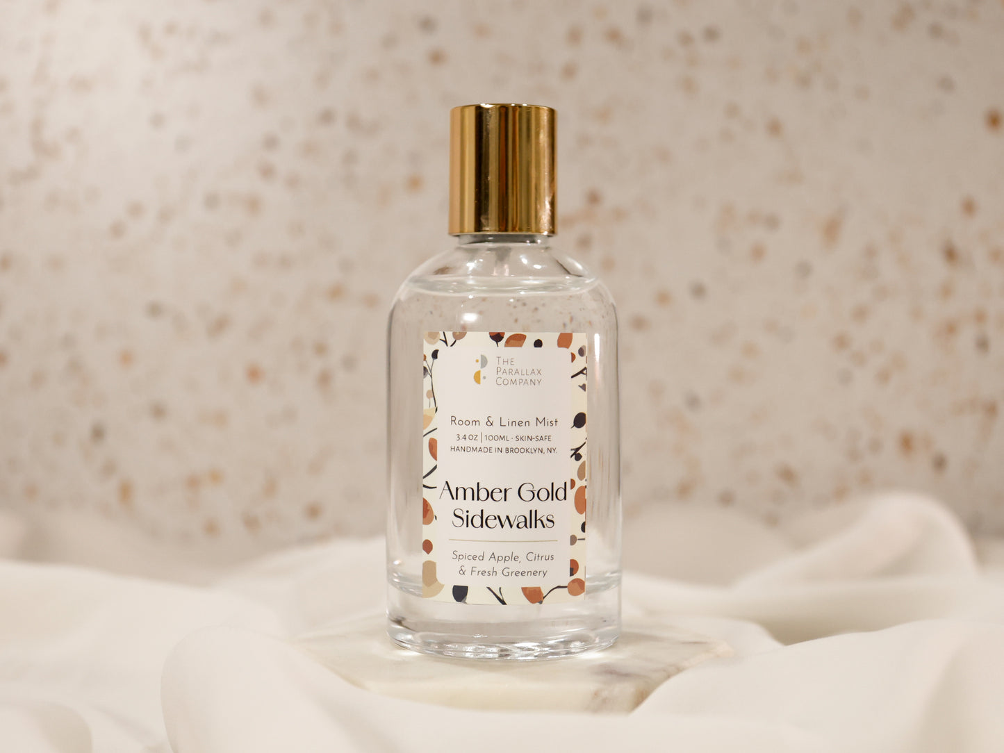 Room and fabric mist bottle of 'Amber Gold Sidewalks’ fragrance in a soft white cloud setup