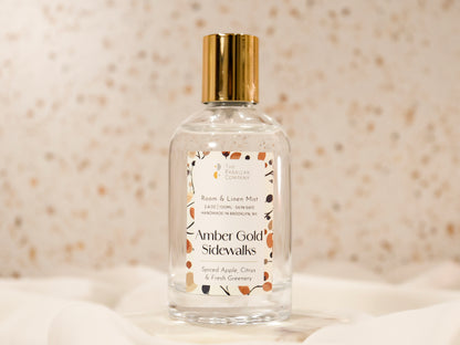 Clear glass bottle with gold cap labeled 'Amber Gold Sidewalks' Room and linen spray mist, handmade in New York