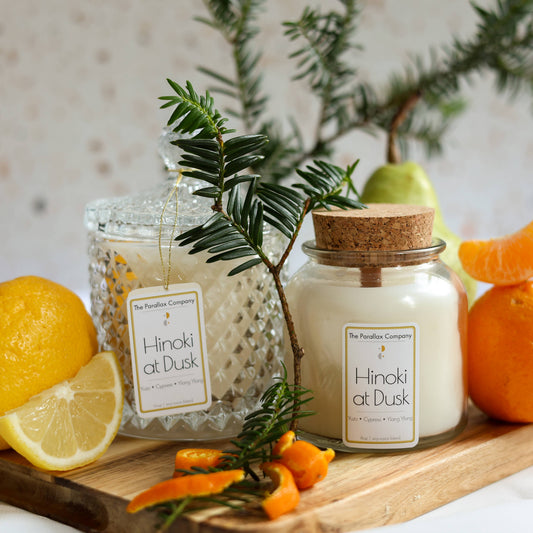 Candles labeled 'Hinoki at Dusk' on wood, with lemons, oranges, orange peels and Japanese cypress.