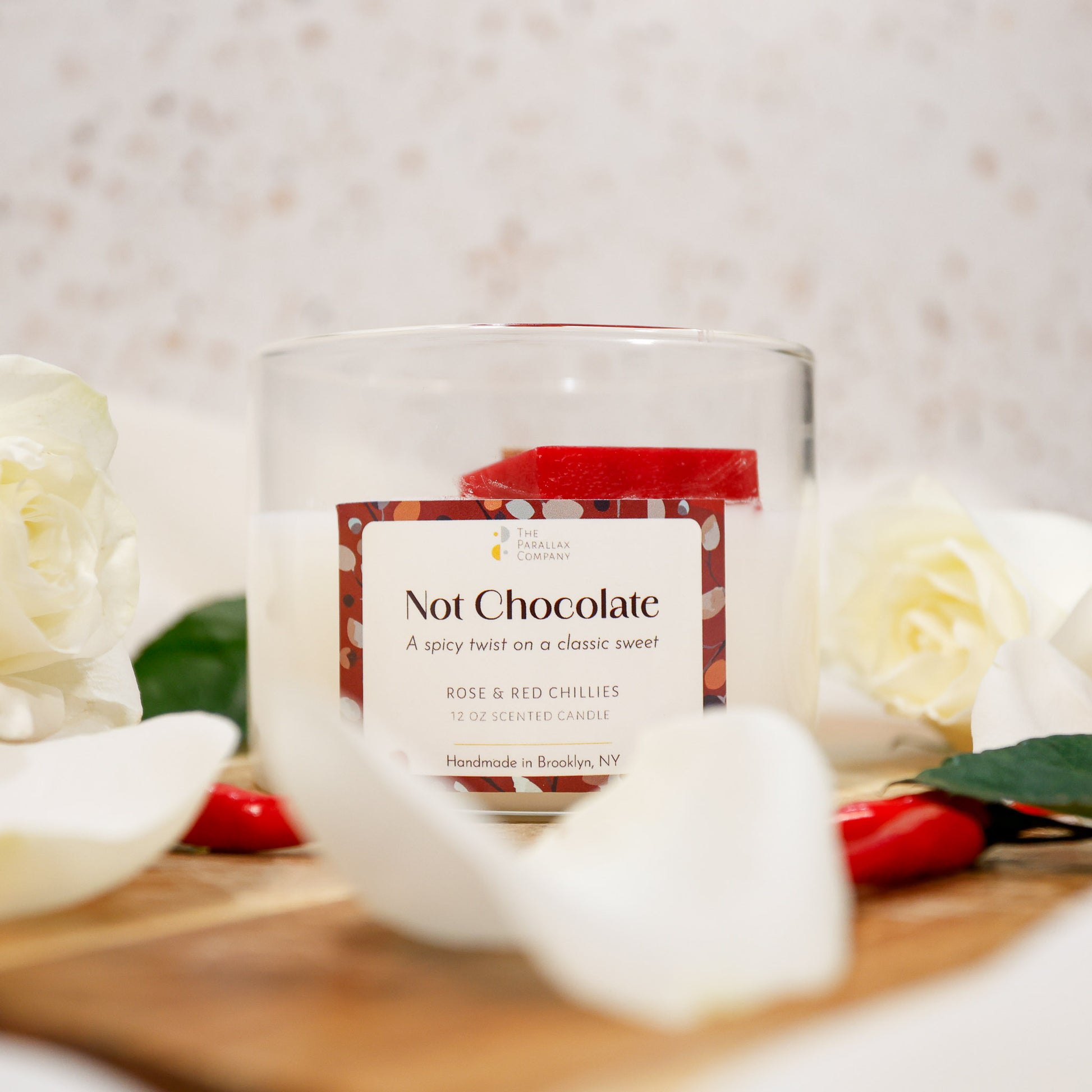Scented candle labeled 'Not Chocolate' with roses and red peppers on a wooden surface
