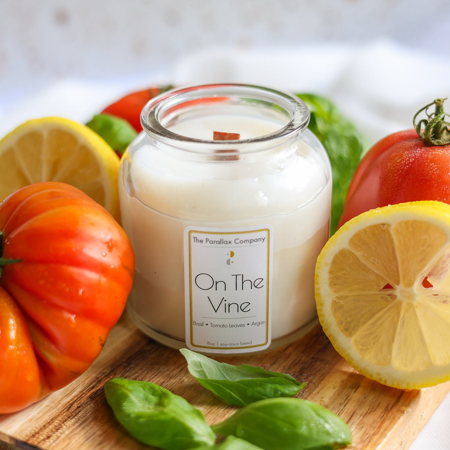 Candle labeled 'On The Vine' surrounded by fresh heirloom tomatoes and lemons on a wooden board.