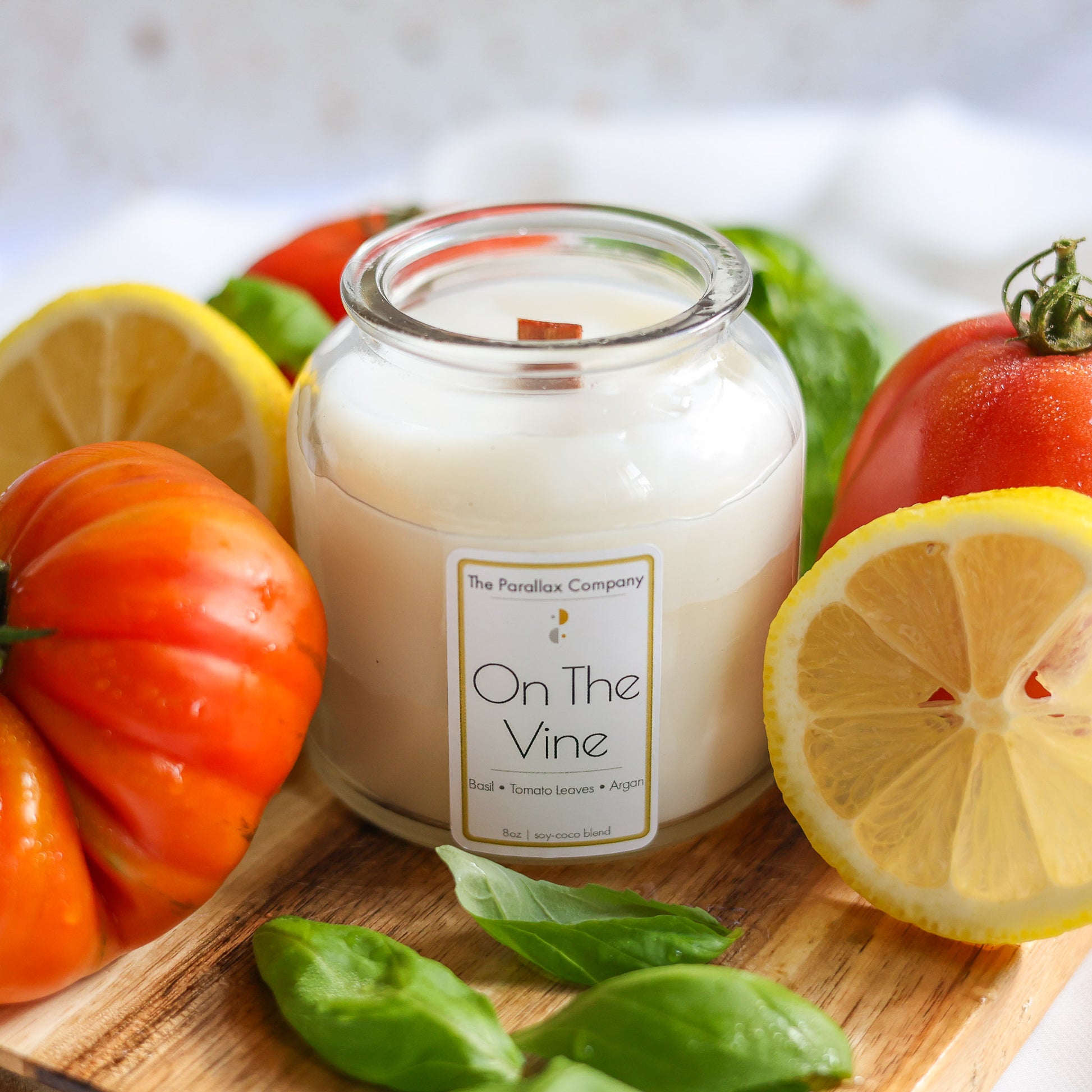 Candle labeled 'On The Vine' surrounded by fresh heirloom tomatoes and lemons on a wooden board.