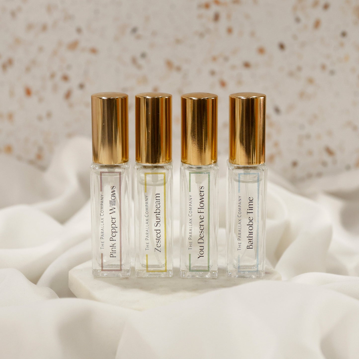 Four small perfume bottles with gold caps on a white fabric background