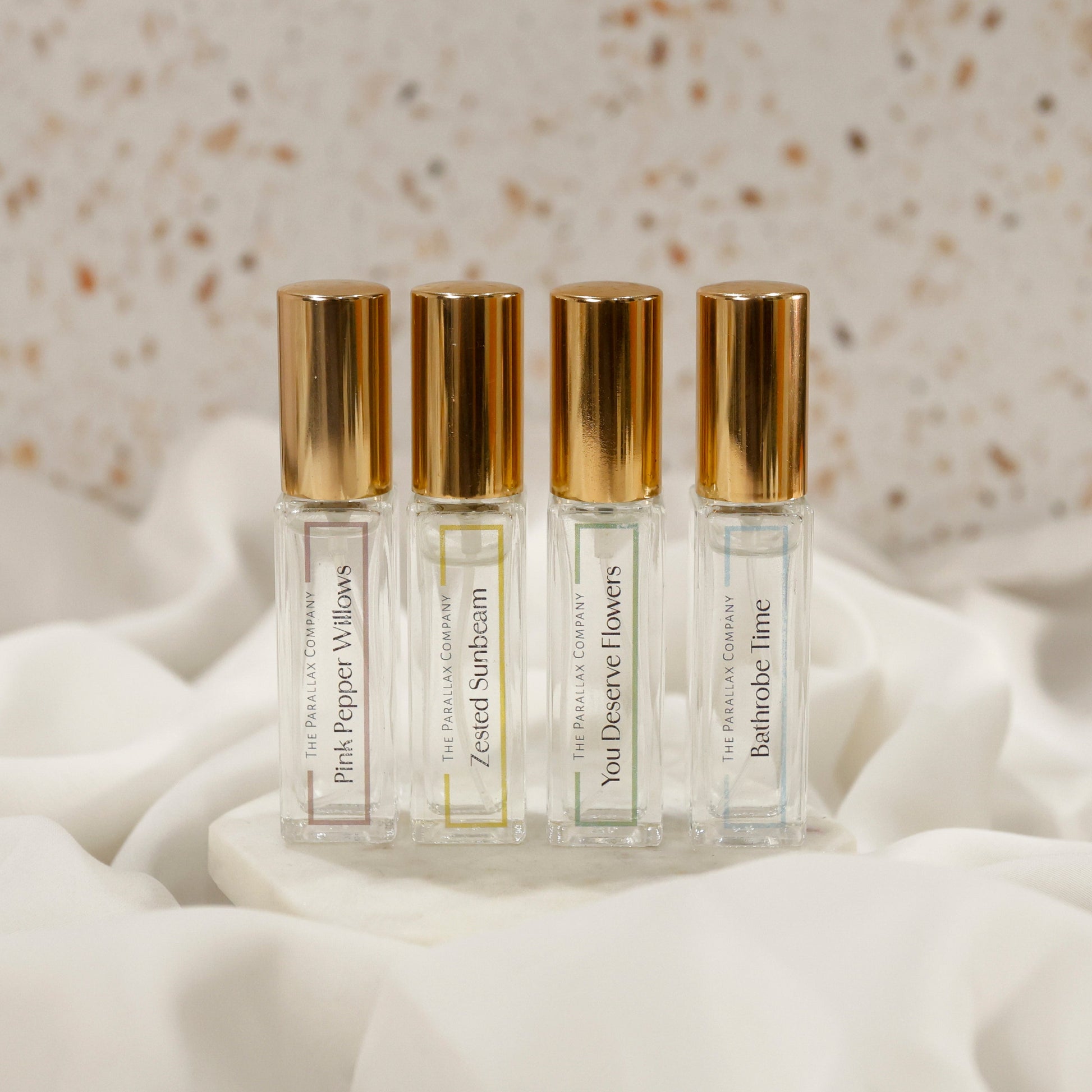 Four small perfume bottles with gold caps on a white fabric background
