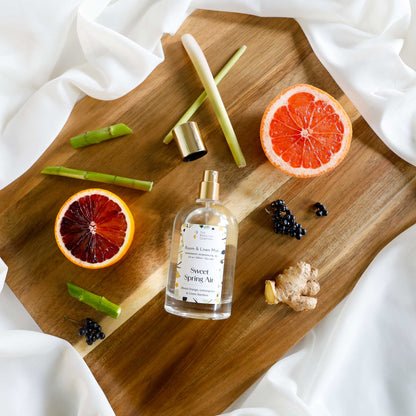 Bottle of Sweet Spring Air room and linen mist on a wooden board with blood orange, lemongrass, grapefruit, fresh green bamboo, ginger, and black currants