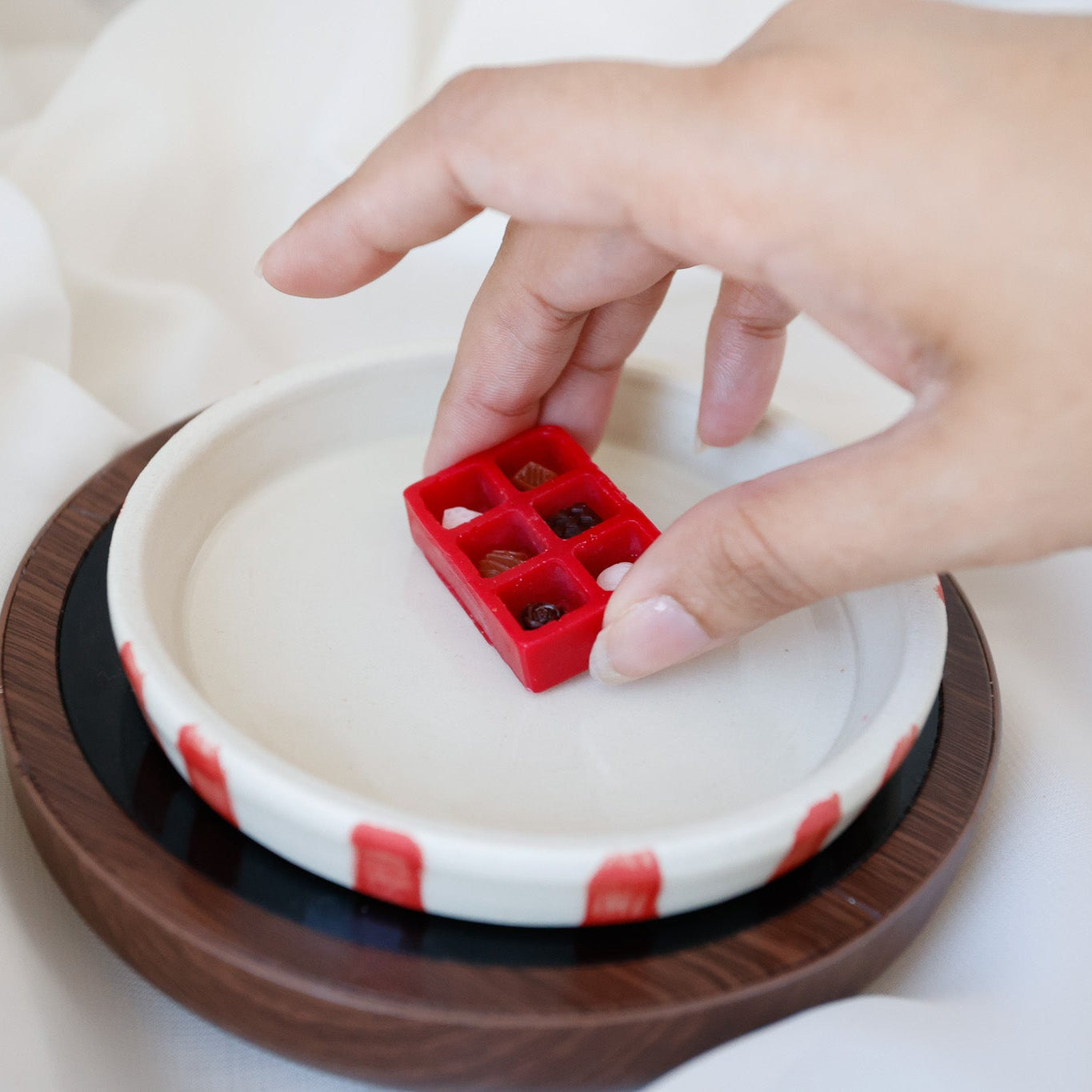 Hand placing a red chocolate box shaped wax melt on a white dish candle warmer.