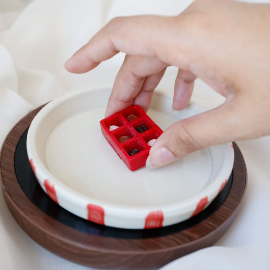 Hand placing a red chocolate box shaped wax melt on a white dish candle warmer.